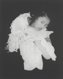 Model in white textured garment with ruffled details looking up against a dark background, styled by Alberto Vegue