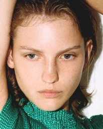 Close-up portrait of a woman with freckles wearing a green knitted sleeveless top, styled by Alberto Vegue.