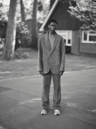Black man standing outdoors wearing a tailored grey suit jacket and trousers styled by Alberto Vegue.