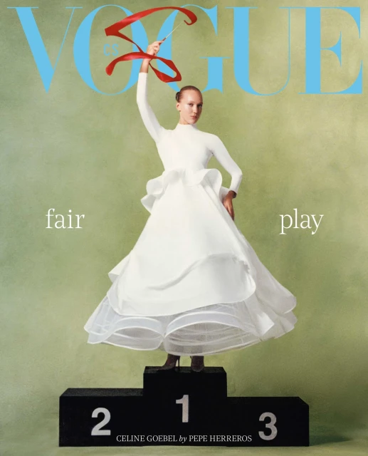 Magazine cover featuring a woman in a white dress on a podium, holding a red ribbon, with the Vogue logo in blue at the top.