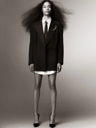 Elegant portrait of a Black woman in a business suit and high heels, standing in front of a neutral backdrop, showcasing fashion and style.