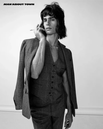 Black and white editorial portrait of a male model with dark hair wearing a patterned vest and suit jacket holding a cigarette