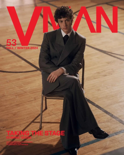 A young man in a suit sits on a chair in a gym for a magazine cover. The cover is red, white and dark colors.