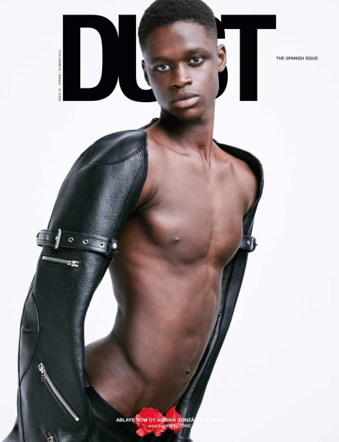 Magazine cover featuring a Black man with a muscular build, wearing black leather sleeves, posing against a bright white backdrop. 