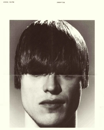 Close-up monochrome portrait of a person with a bowl cut obscuring their eyes against a neutral background.
