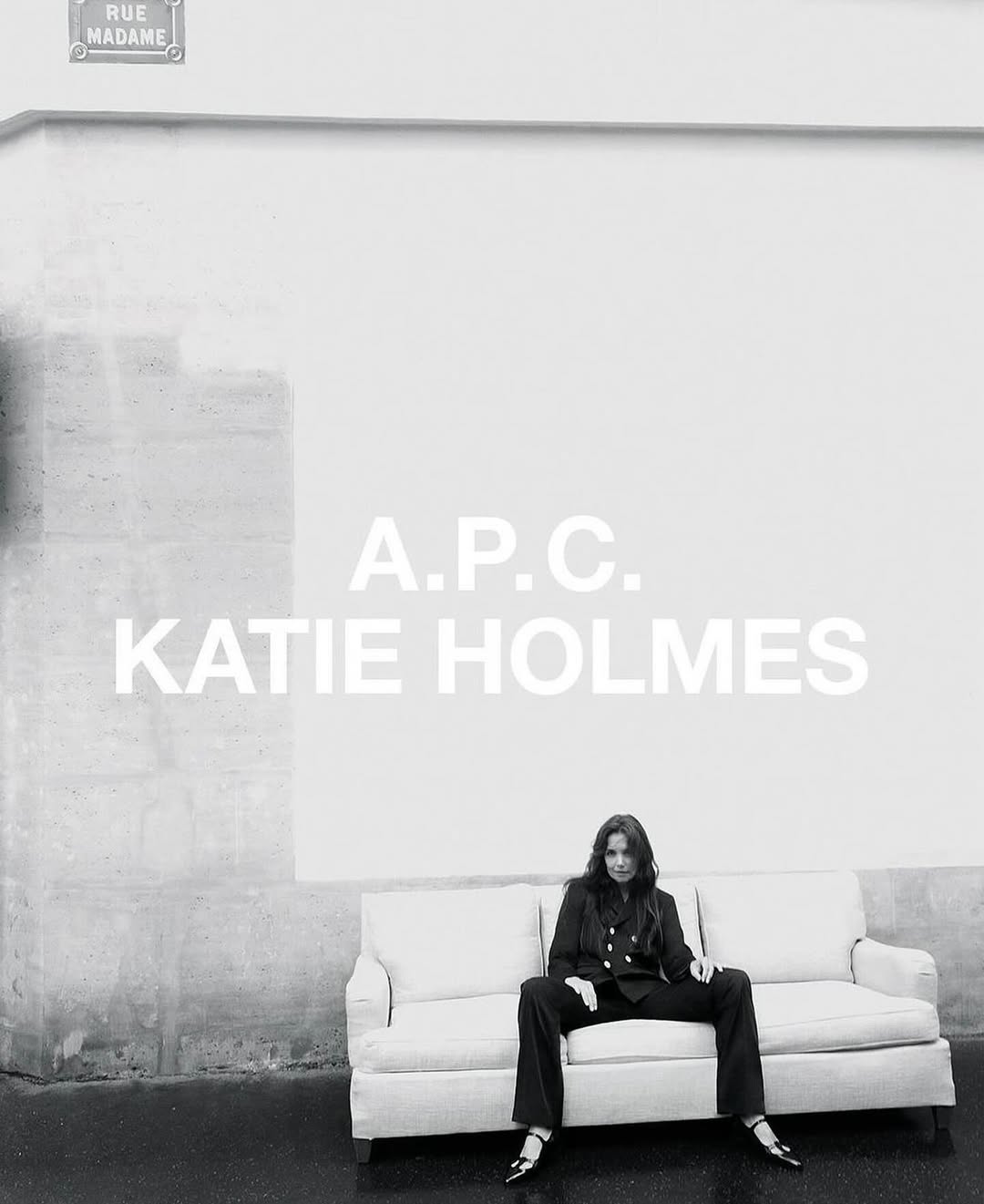 Katie Holmes seated on a light sofa outdoors in front of a white wall, styled by Charlotte Collet.