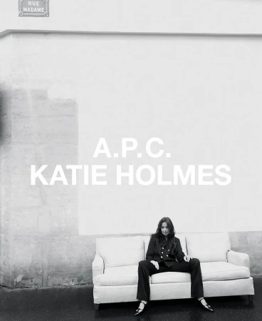 Katie Holmes seated on a light sofa outdoors in front of a white wall, styled by Charlotte Collet.