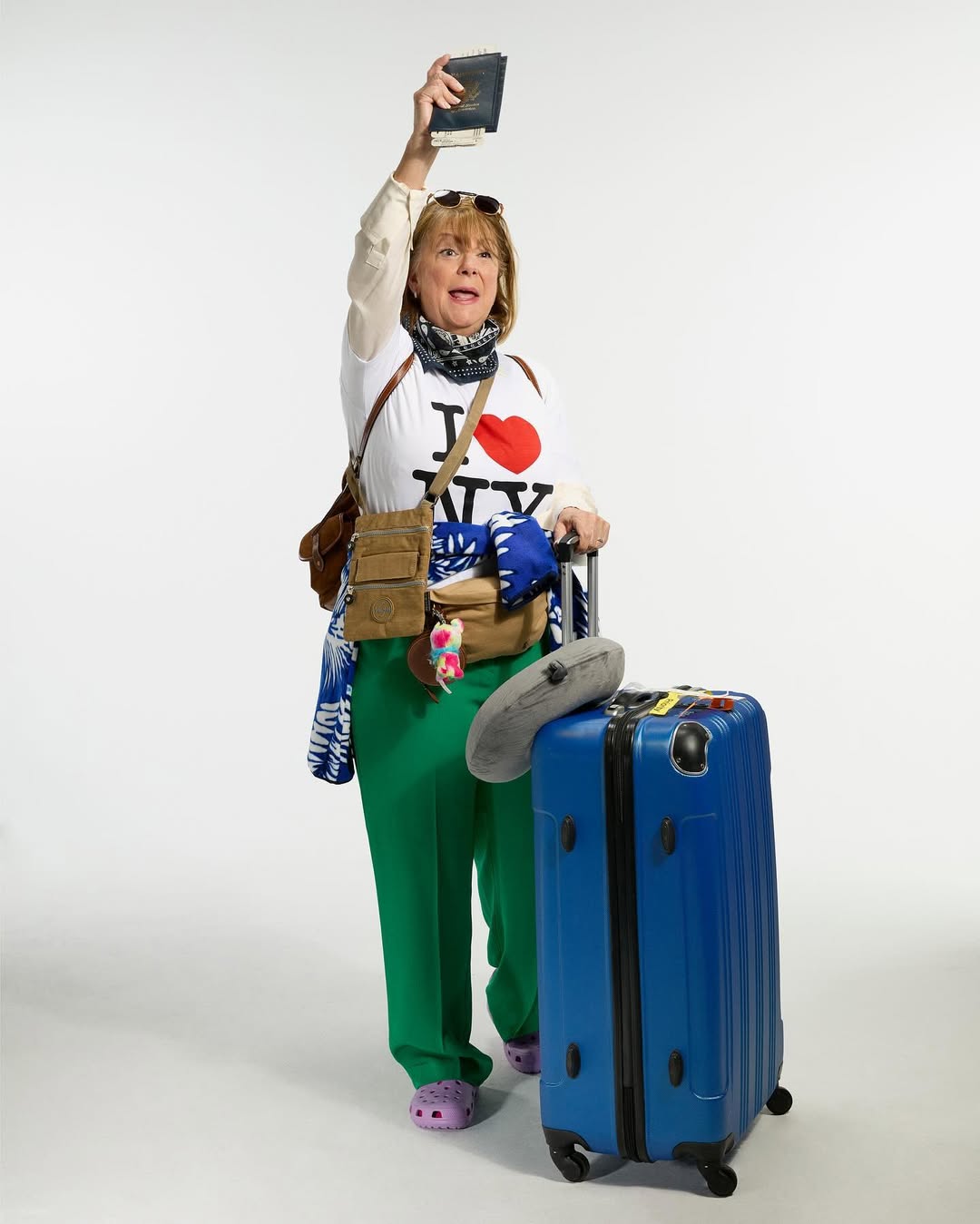 Full shot of a mature woman in travel attire, holding a passport, standing with a suitcase, expressing excitement on a white background.
