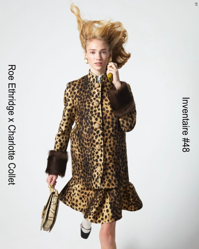 A woman in a vintage animal print skirt suit and Mary Janes holds a yellow object and a purse against a white background.