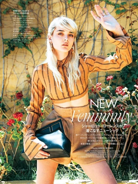 Fashion editorial shot of a fair-skinned woman with blonde hair wearing a tan striped crop-top and shorts holding a black purse.