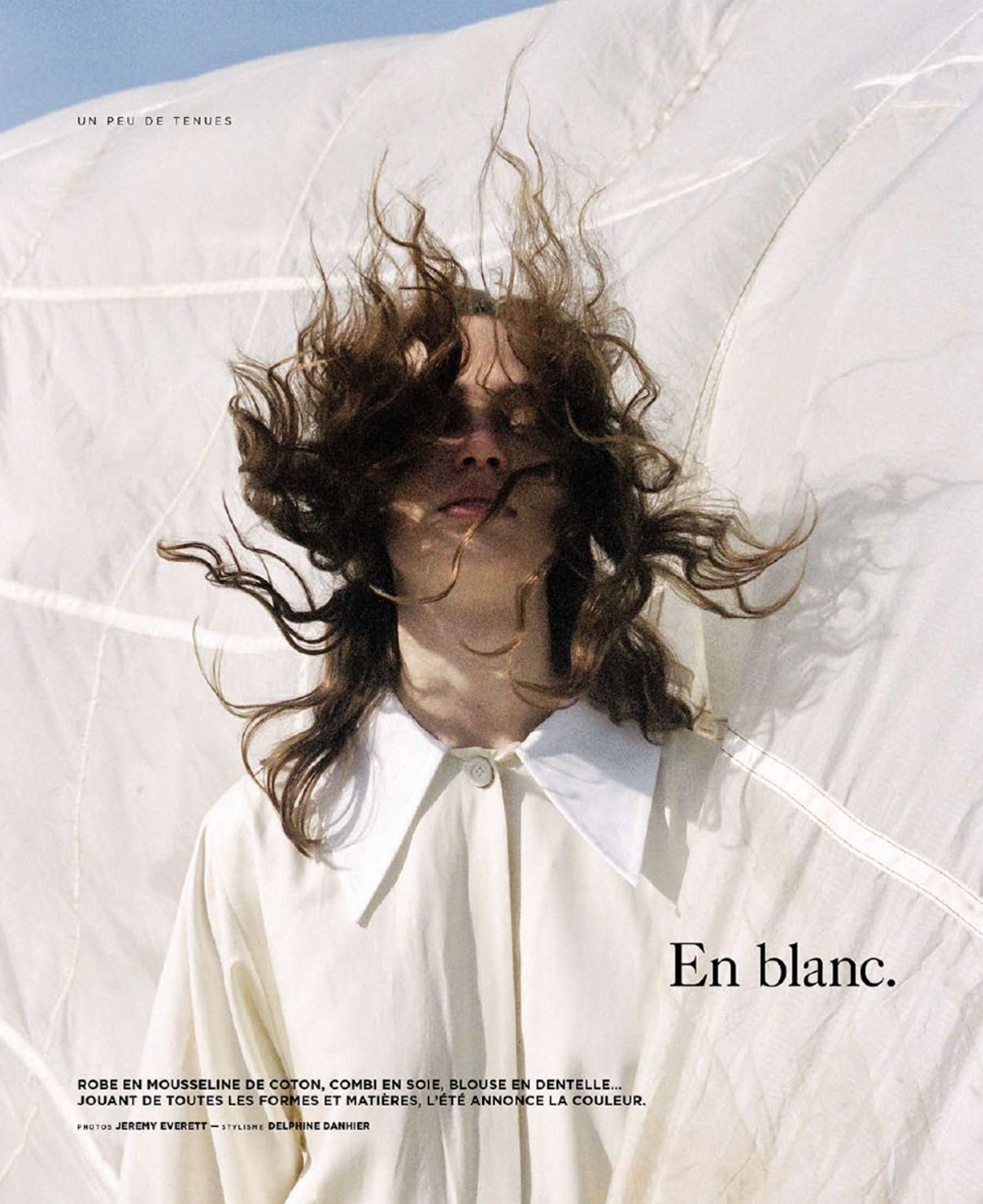 Fashion editorial featuring a fair-skinned person with long, wavy brown hair, wearing a light shirt, against a blurred white background.
