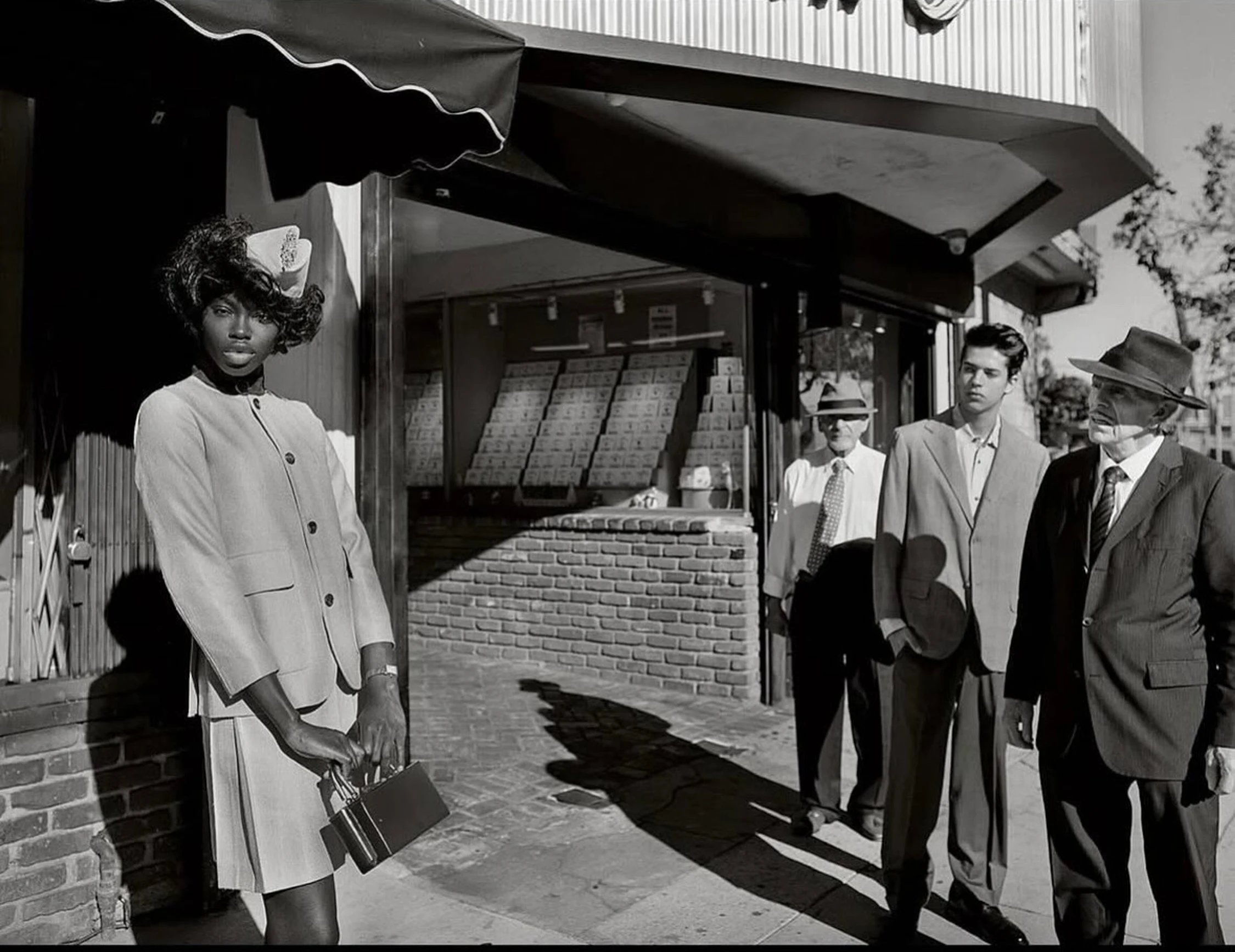 Monochrome portrait of a stylish African American woman in suit, holding a purse outside a store, with three men in the background.
