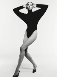 Model in black bodysuit posing with hands on head against white background with make-up by John Mckay