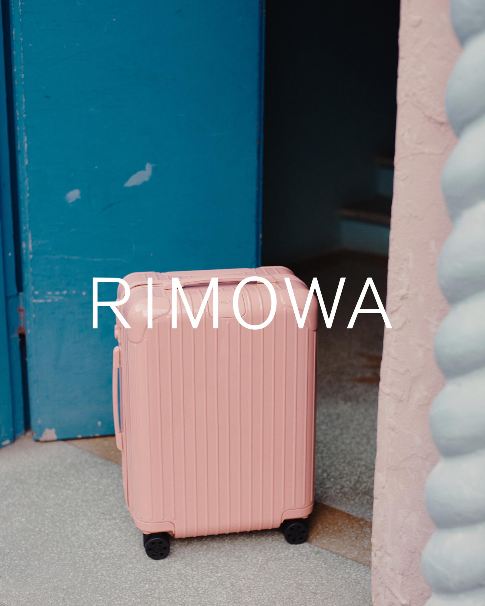 Coral pink Rimowa suitcase positioned in front of a turquoise door and a light pink wall, creating a vibrant and modern travel image.