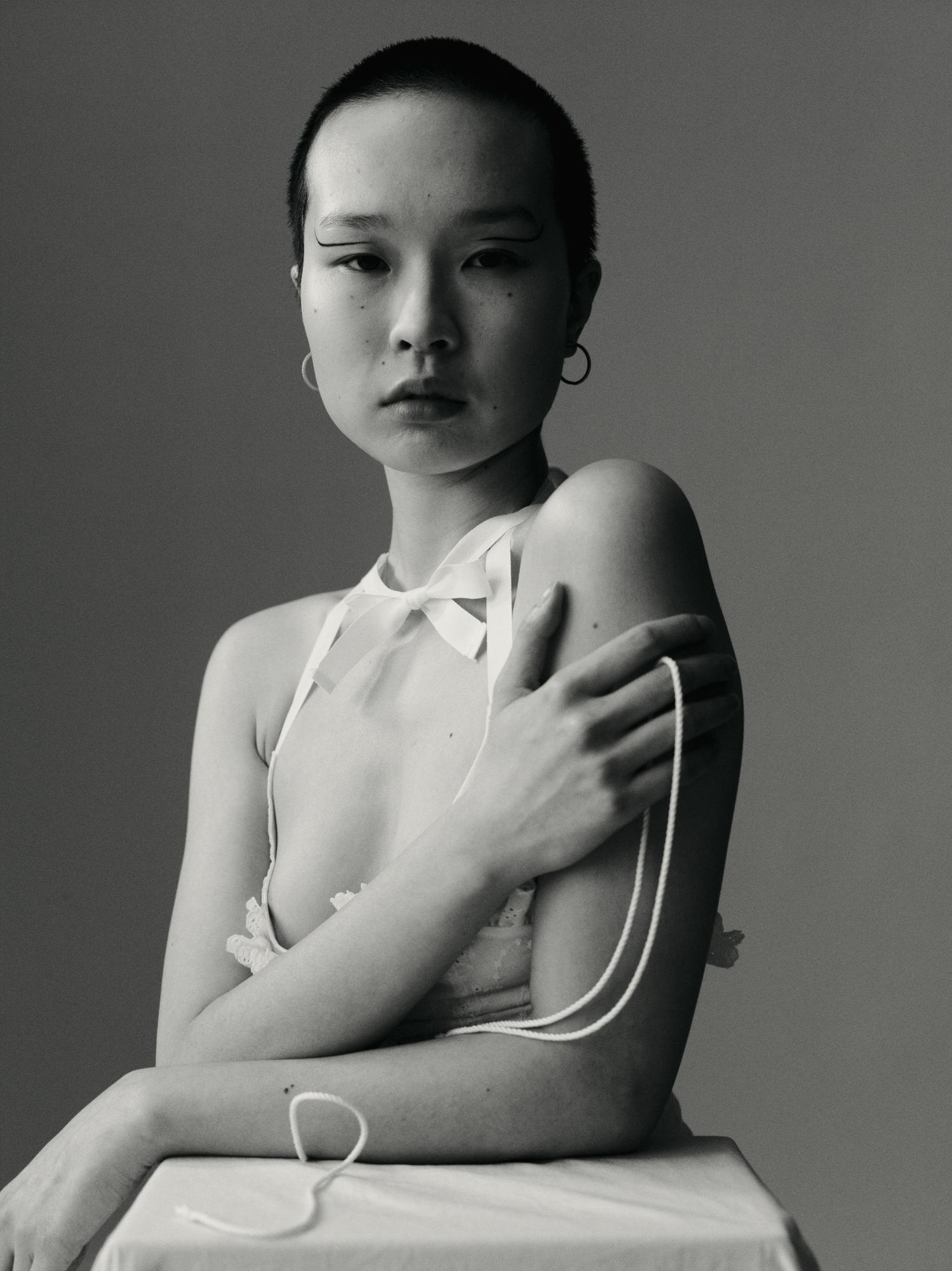 Elegant black and white portrait of an Asian woman with short hair wearing a sheer top with white string, posing in a studio.
