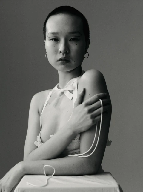 Elegant black and white portrait of an Asian woman with short hair wearing a sheer top with white string, posing in a studio.