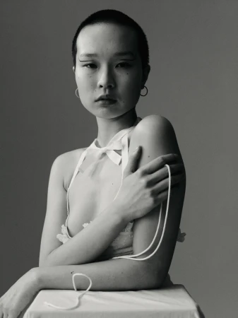 Elegant black and white portrait of an Asian woman with short hair wearing a sheer top with white string, posing in a studio.
