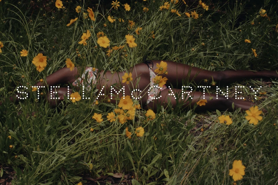 Woman in floral bikini lies in field of Coreopsis flowers, shadowed light, 'Stella McCartney' text overlay, fashion, beauty, nature theme.