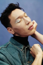 Portrait of a man with closed eyes wearing a denim jacket and dark turtleneck against a blue background, by James Tolich