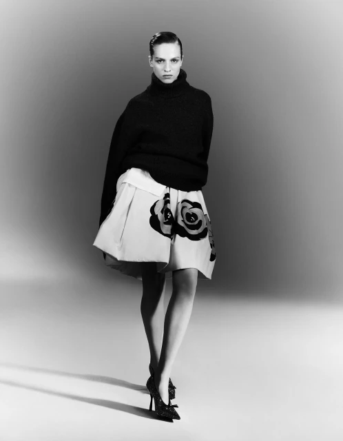 Elegant fashion shot: Woman in black turtleneck and floral skirt poses in a studio, blending modern style with a classic black-and-white aesthetic.