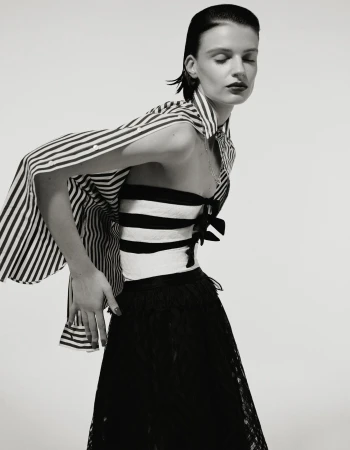 Monochrome portrait of a woman in a striped top and lace skirt, posing in front of a white backdrop in a fashion editorial style.