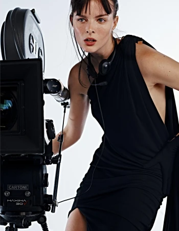 Woman in black dress poses with a vintage film camera in a studio setting, creating a striking fashion image.
