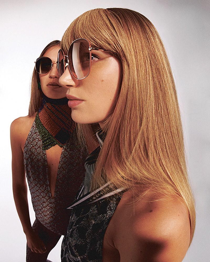 Two models wearing oversized sunglasses and patterned tops against a plain white background by Dora Roberti.