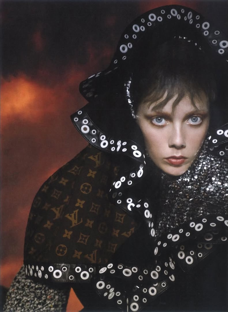 Portrait of a woman with blue eyes in a black hat and patterned top in a dark photo studio with orange and black background.