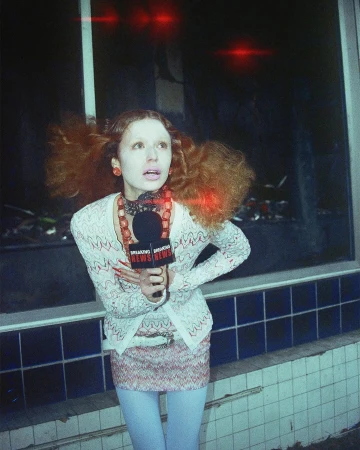 Woman holding a 'Breaking News' microphone stands near a blue-tiled wall, wearing a knitted jacket, mini skirt and light blue leggings.