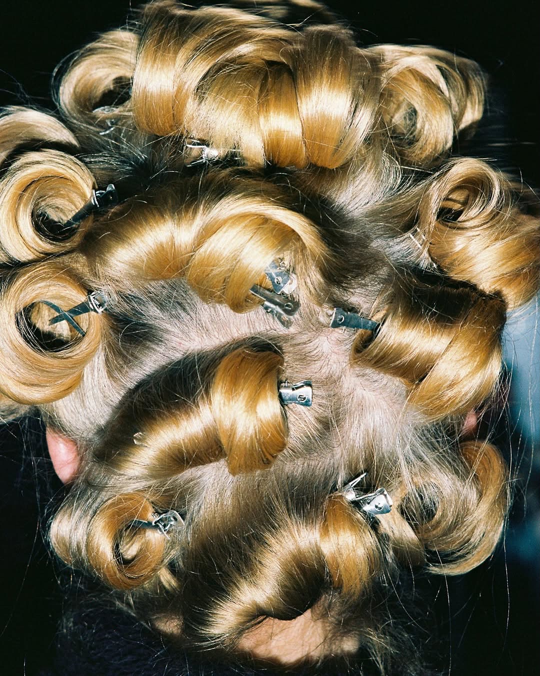 Close-up from behind of blonde hair styled in voluminous curls and secured with metal clips, showcasing a beauty and hairstyling aesthetic.