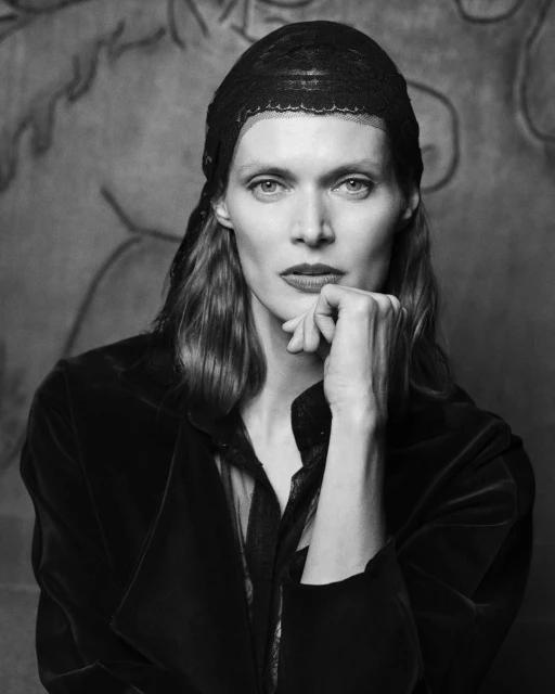 Monochrome portrait of an adult female model with a black lace headscarf, wearing a dark velvet jacket, resting her chin on her hand.