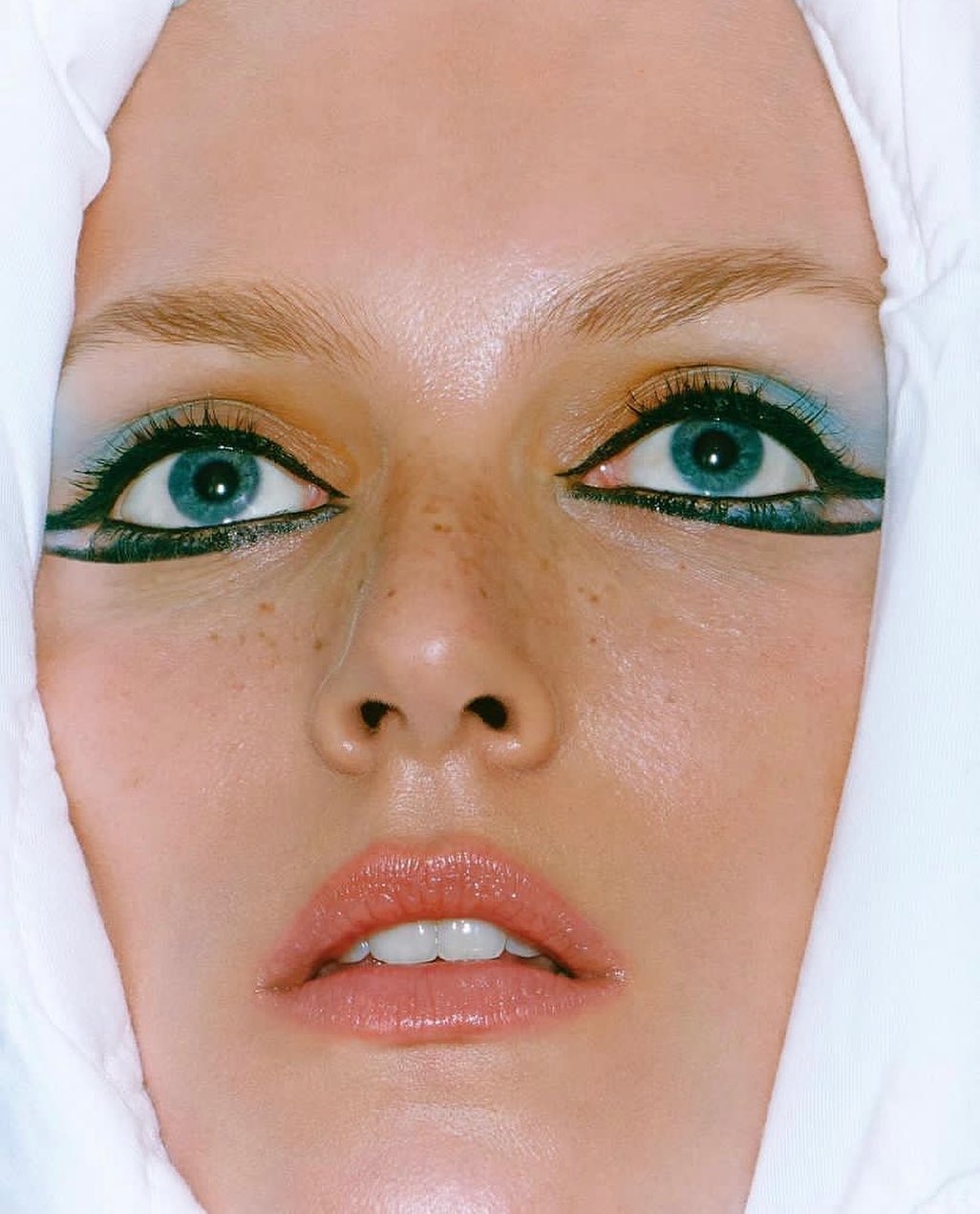 Close-up portrait of a woman with striking blue eyes and unique makeup, wearing a white head covering, beauty, and fashion.