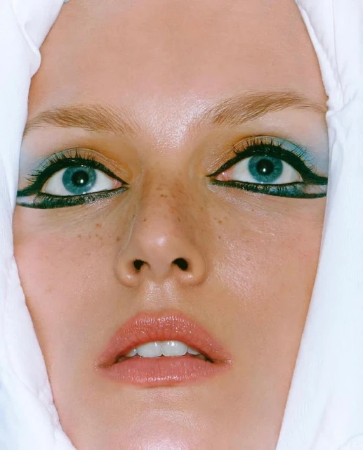 Close-up portrait of a woman with striking blue eyes and unique makeup, wearing a white head covering, beauty, and fashion.