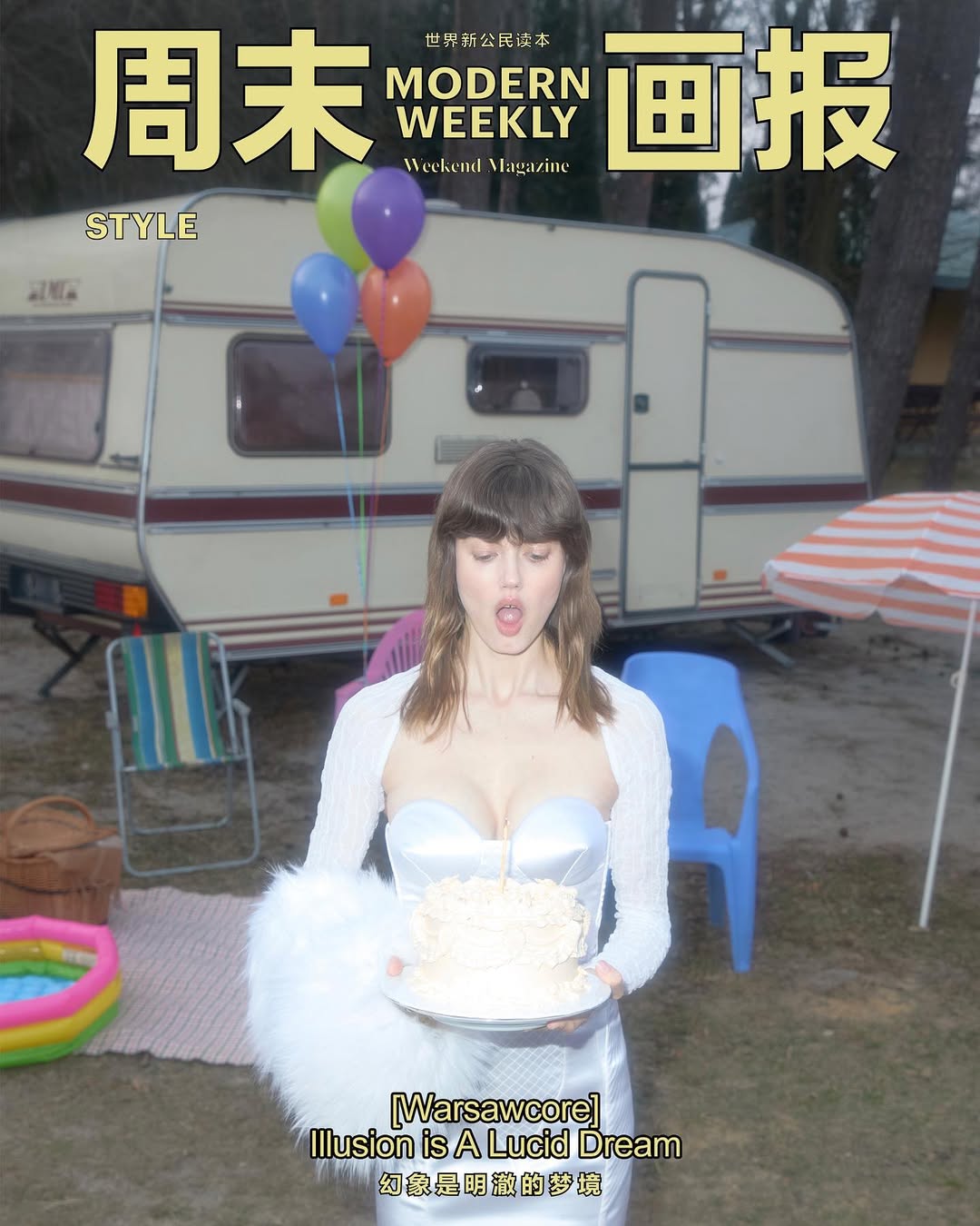Editorial fashion shot of a woman in a white dress holding a cake in front of a vintage camper with balloons and picnic accessories.