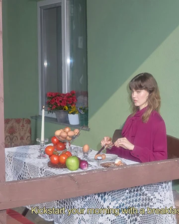 Woman in magenta blouse prepares breakfast outdoors, featuring eggs, tomatoes, and flowers, with an open window in the background.