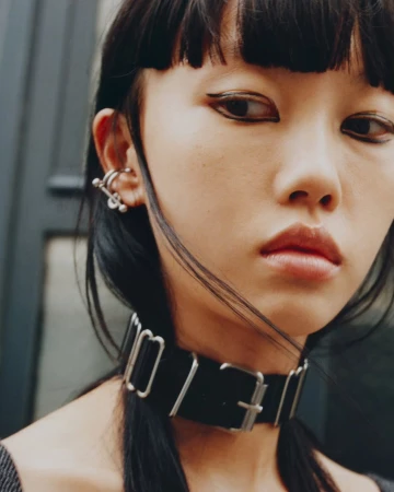 Close-up portrait of a woman wearing graphic eyeliner, a thick black buckled choker, and silver ear cuffs by makeup artist Marianna Yurkiewicz