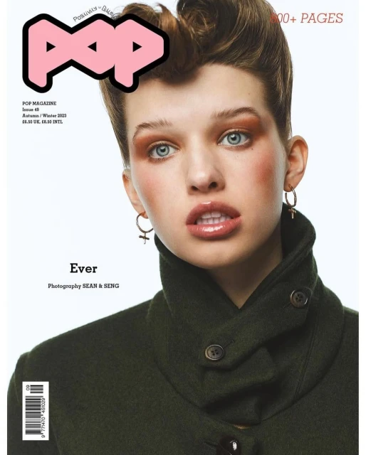 Fashion magazine cover featuring a woman with auburn hair and green coat, wearing hoop earrings with cross charms in a bright, studio setting.