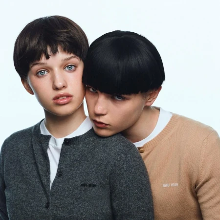 Two models with short bowl-cut hairstyles posing closely against a plain white background, wearing knit sweaters.