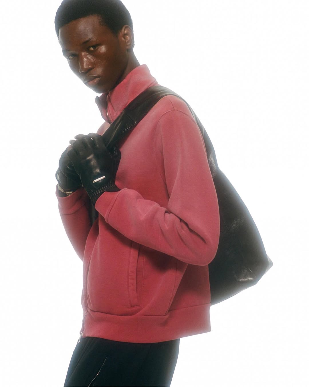 Man in pink jacket and black gloves carries bag in a clean studio shot with a bright white background. Fashion portrait.