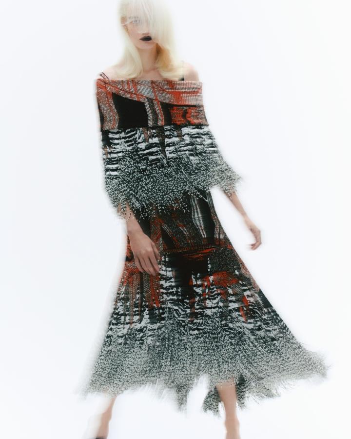 Fashionable woman posing in a patterned fringe dress in a brightly lit studio. The image showcases a blend of texture, color, and style.