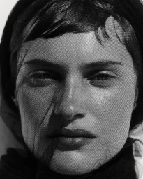 Close-up portrait of a woman wearing a black mesh veil over her face in monochrome style.