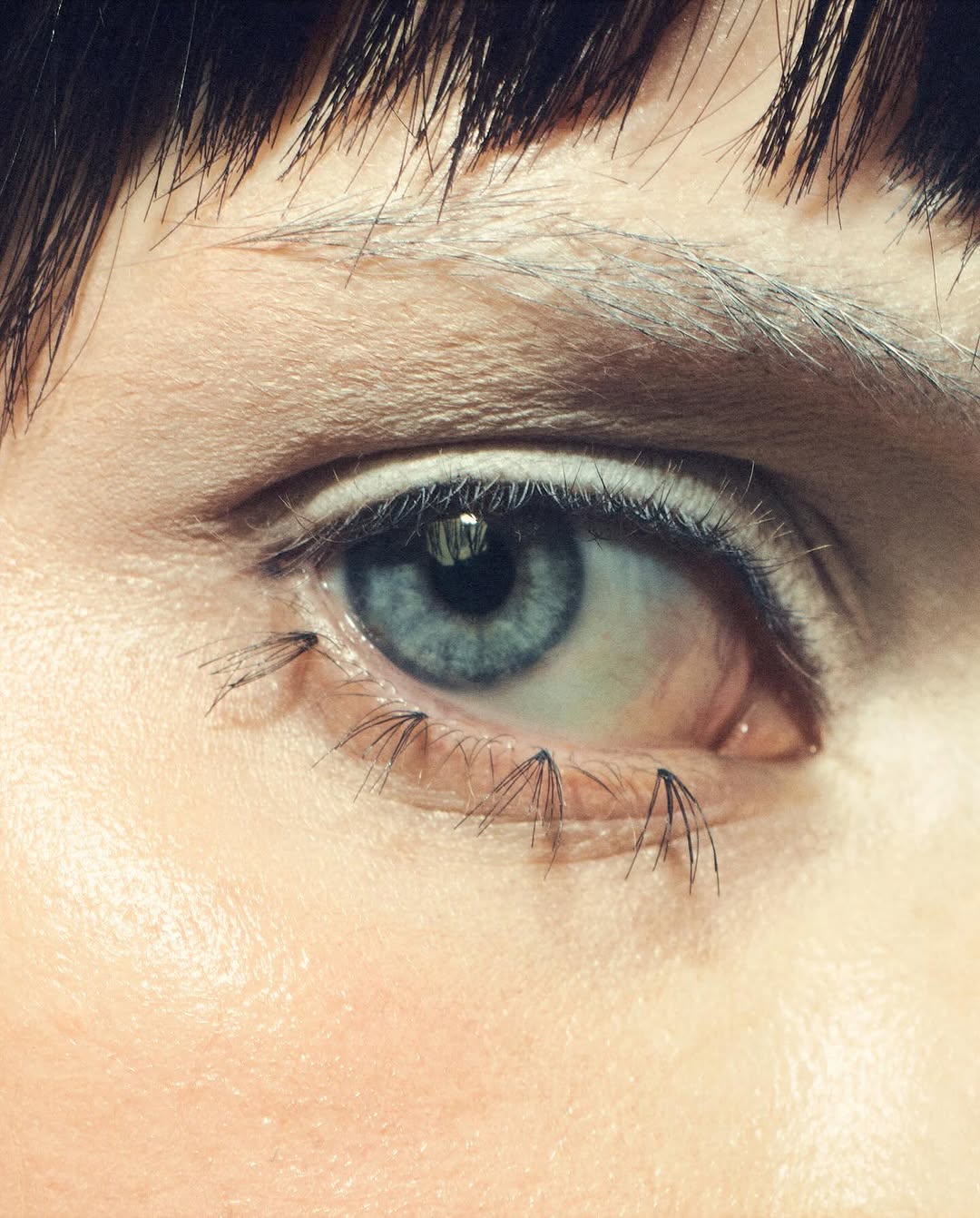 Close-up on a blue eye with creative eyelash extensions resembling spider legs, set against fair skin and dark hair.