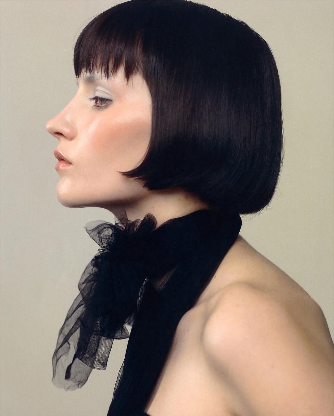 Profile of adult woman with dark bob haircut and wearing a black scarf on beige background in portrait format. Fashion and beauty shot.