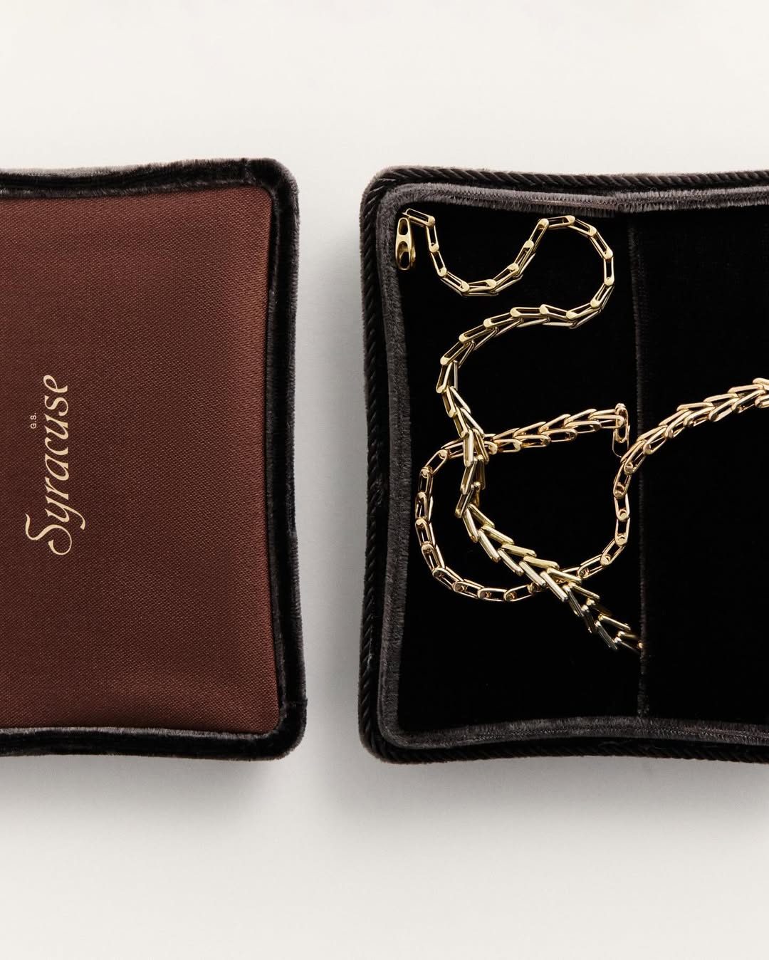 Gold chain necklace displayed inside a black velvet jewelry box, with the brand name 'Syracuse' visible on a brown box to the left.