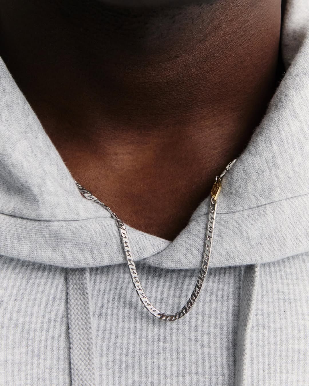 Close-up of a person wearing a gray hooded sweatshirt and a silver chain necklace, showcasing fashion and personal style.