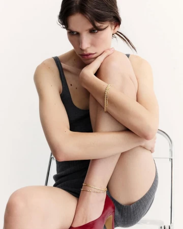 Woman in dark grey tank top and red high heels sitting on a chair against a white background