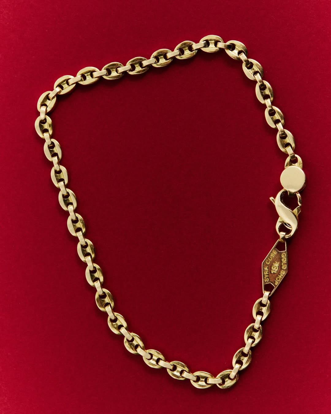 Close-up of a gold chain necklace jewelry, laid out on a dark red background. The chain has lobster clasp closure.