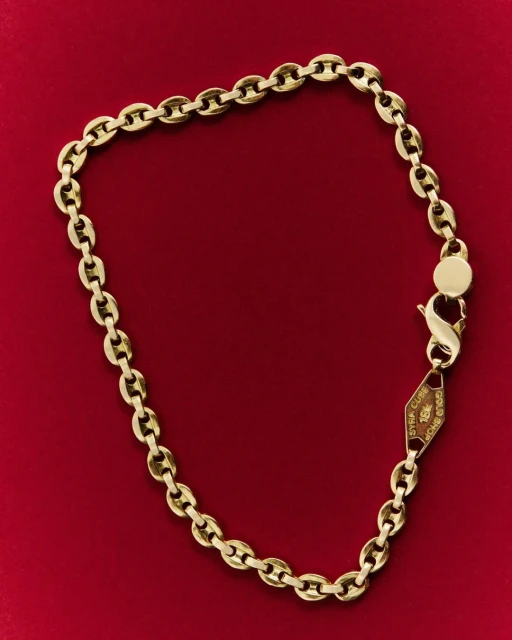 Close-up of a gold chain necklace jewelry, laid out on a dark red background. The chain has lobster clasp closure. 