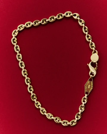 Close-up of a gold chain necklace jewelry, laid out on a dark red background. The chain has lobster clasp closure. 