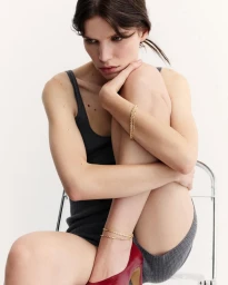 Woman in dark grey tank top and red high heels sitting on a chair against a white background